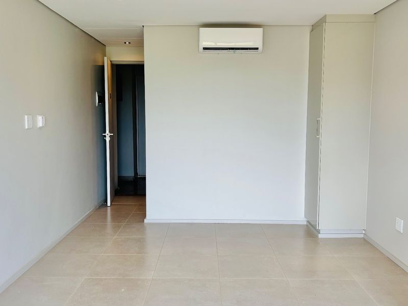 An open-plan living area featuring neutral tiled flooring, a wall-mounted air conditioning unit, and built-in storage cabinetry.