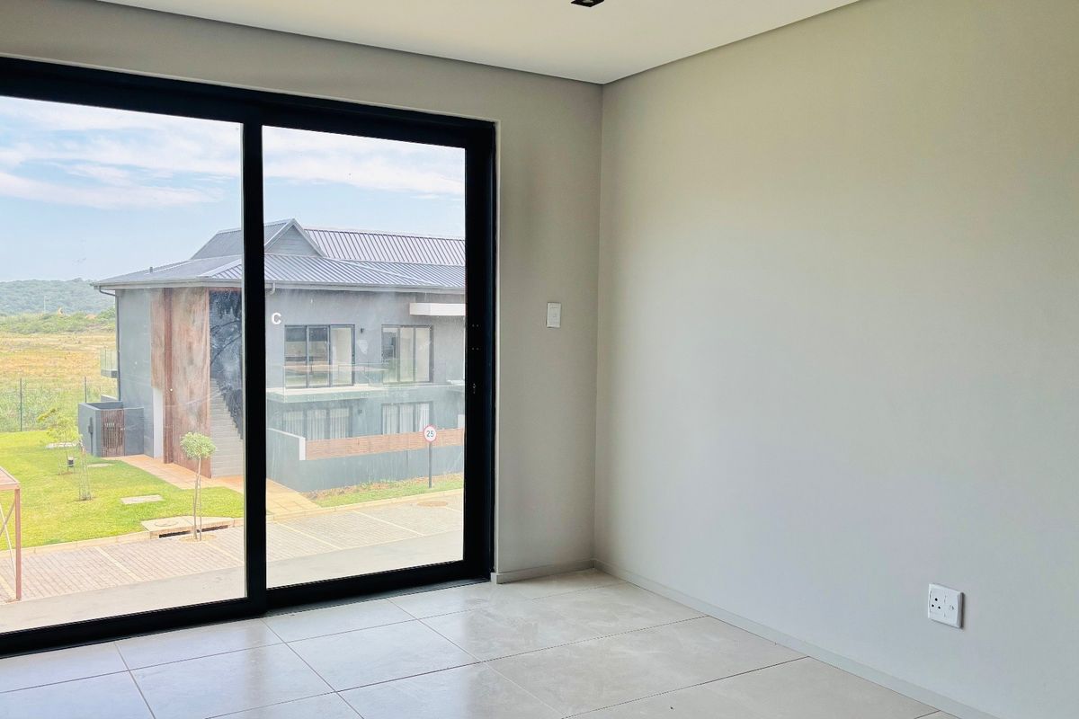 A bright, empty living area featuring large sliding glass doors, neutral tiled flooring, and modern recessed lighting, offering a clean and versatile space.