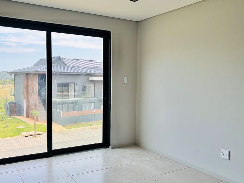 A bright, empty living area featuring large sliding glass doors, neutral tiled flooring, and modern recessed lighting, offering a clean and versatile space.