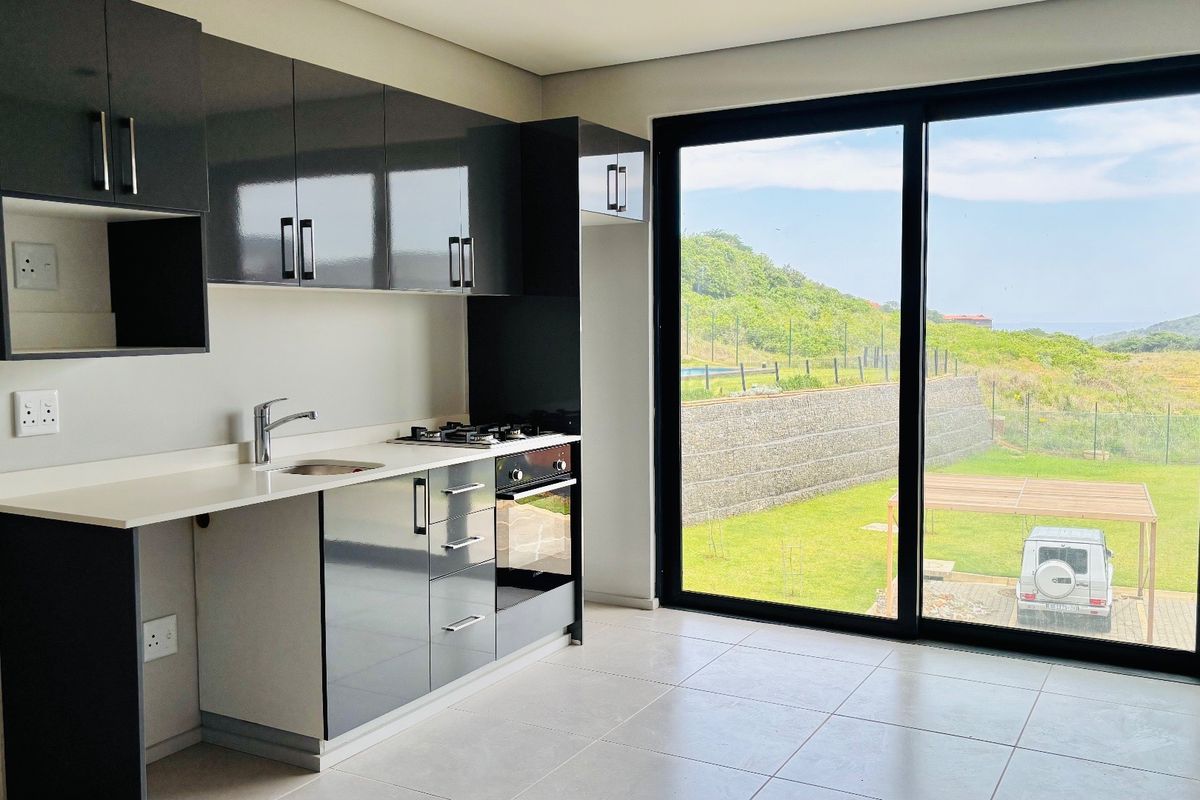 Modern kitchen featuring sleek dark cabinetry, built-in gas hob and oven, and large sliding glass doors opening to a scenic outdoor view.