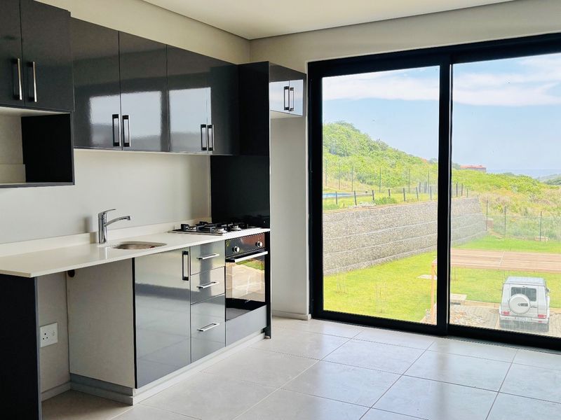 Modern kitchen featuring sleek dark cabinetry, built-in gas hob and oven, and large sliding glass doors opening to a scenic outdoor view.