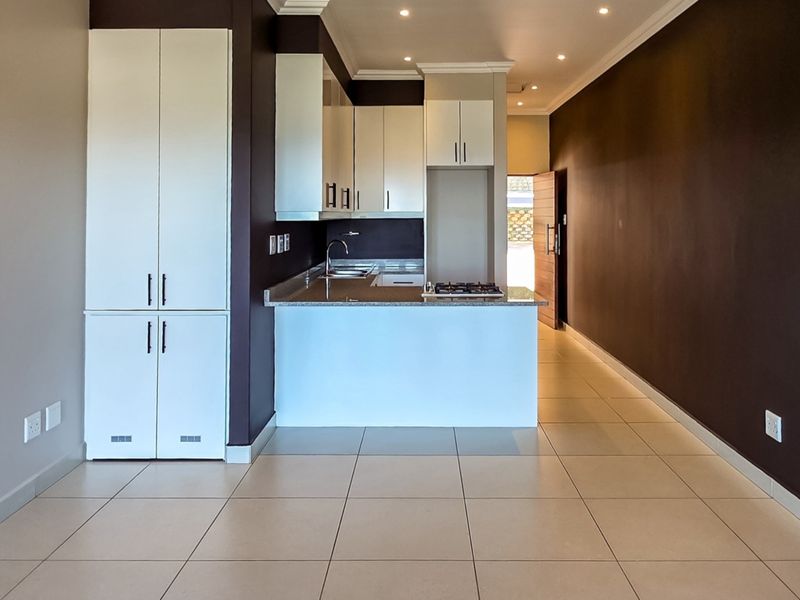 Modern open-plan kitchen featuring white cabinetry, granite countertops, and a gas hob, seamlessly integrated into a spacious living area with tiled flooring.