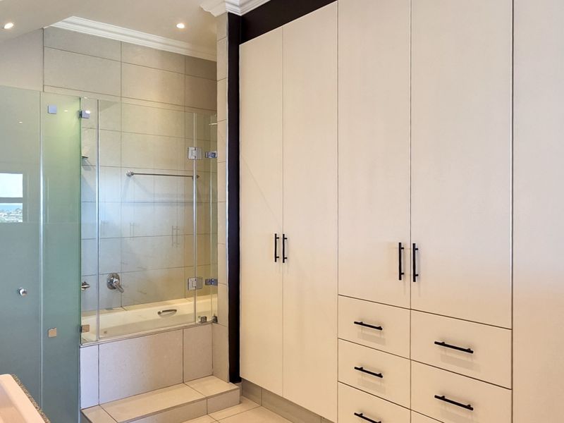 Modern bathroom featuring extensive built-in cabinetry, a bathtub with a glass screen, and neutral tiling throughout.