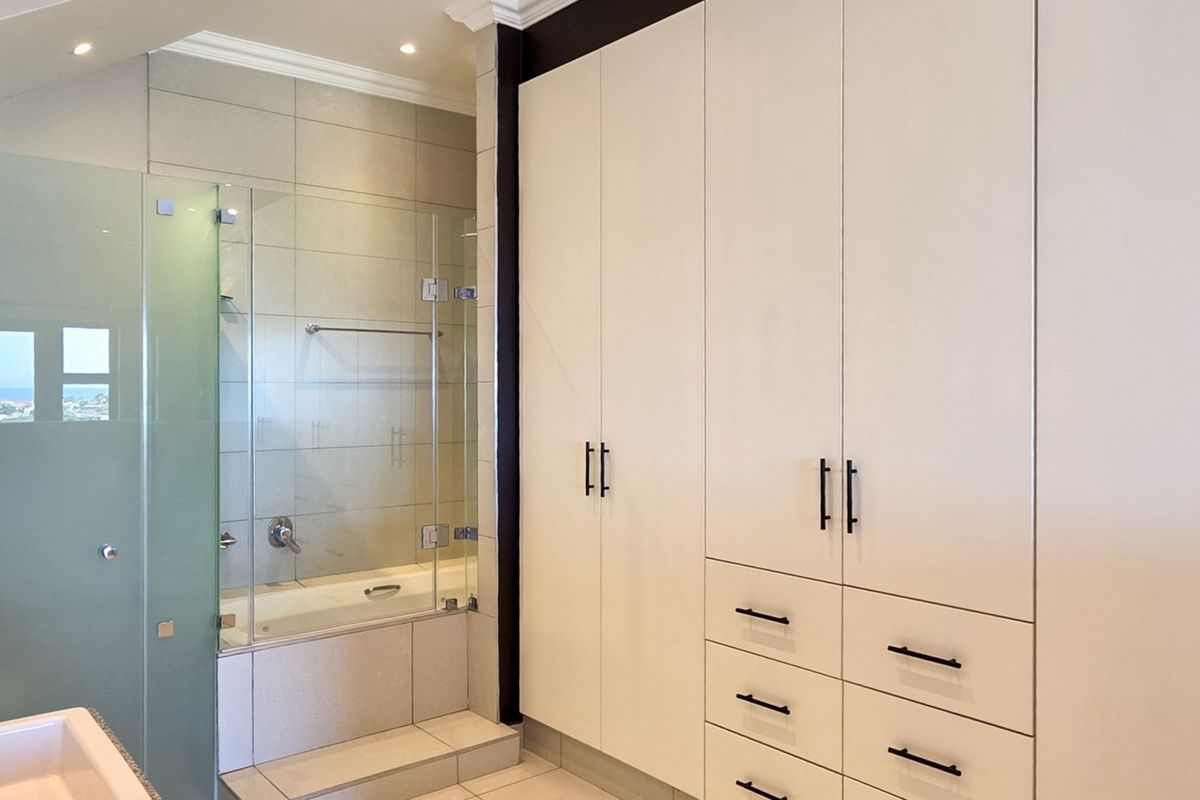 Modern bathroom featuring extensive built-in cabinetry, a bathtub with a glass screen, and neutral tiling throughout.