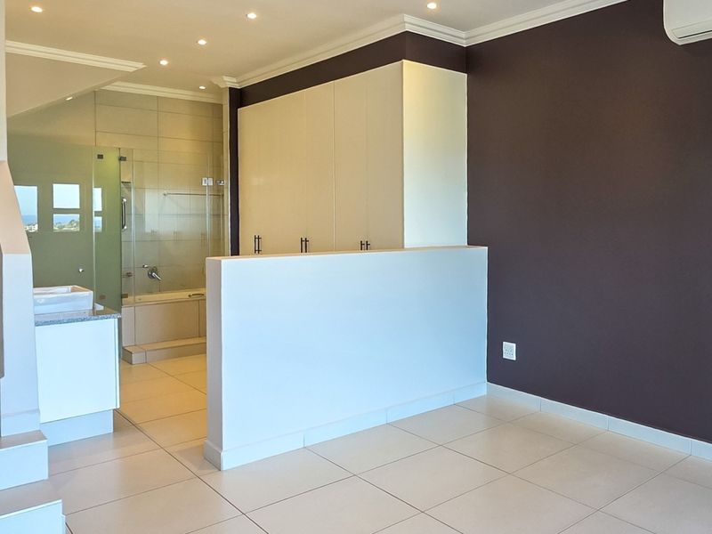 Spacious bedroom featuring an open-plan en-suite bathroom, built-in cupboards, tiled flooring, and a private staircase leading to another level.