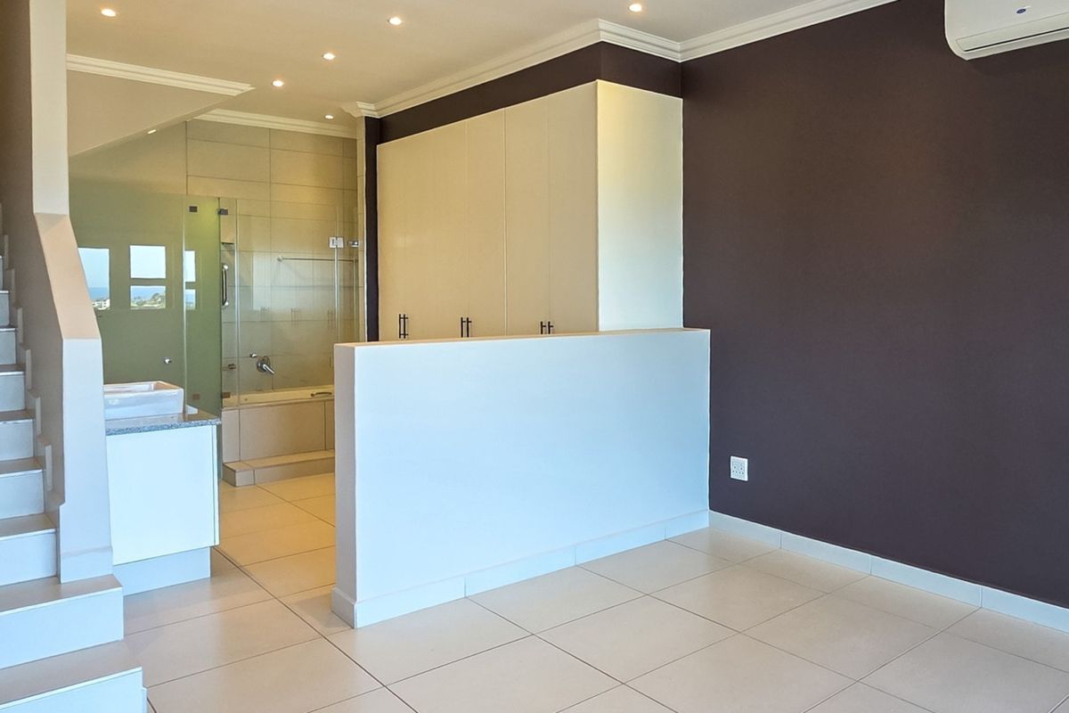 Spacious bedroom featuring an open-plan en-suite bathroom, built-in cupboards, tiled flooring, and a private staircase leading to another level.