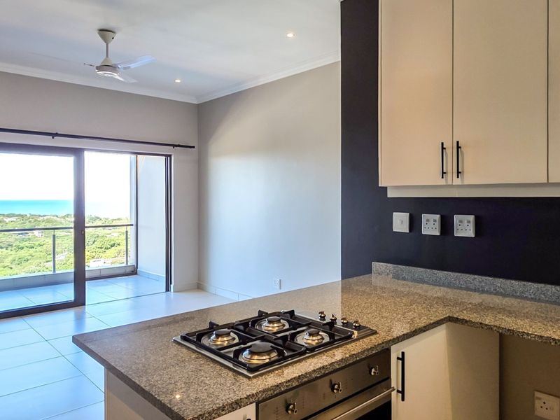 Modern open-plan kitchen featuring granite countertops, built-in gas hob and oven, flowing into a bright living area with access to a balcony with views.