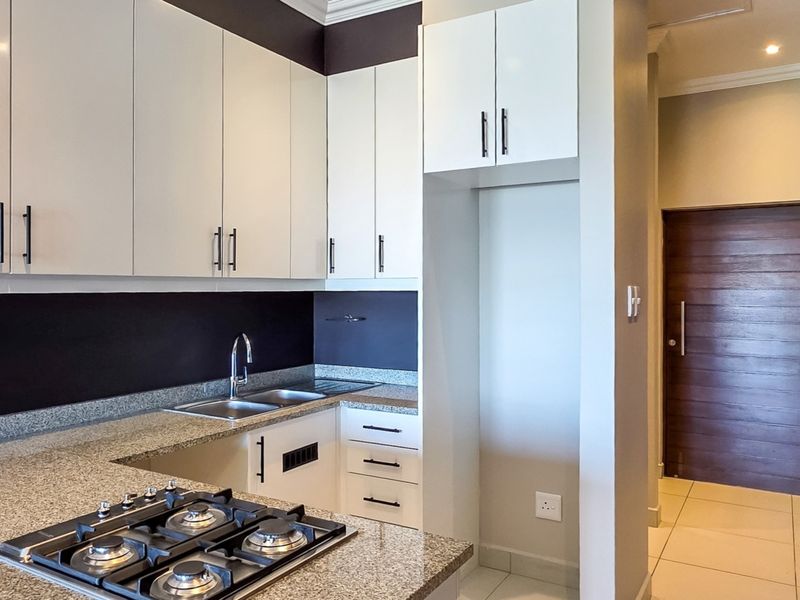 Modern kitchen featuring granite countertops, built-in gas hob, stainless steel sink, and ample cabinetry, finished with neutral tiled flooring.