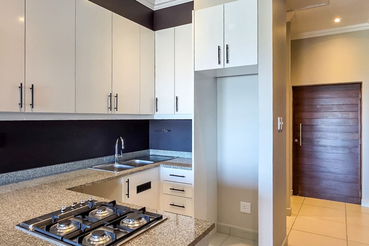 Modern kitchen featuring granite countertops, built-in gas hob, stainless steel sink, and ample cabinetry, finished with neutral tiled flooring.