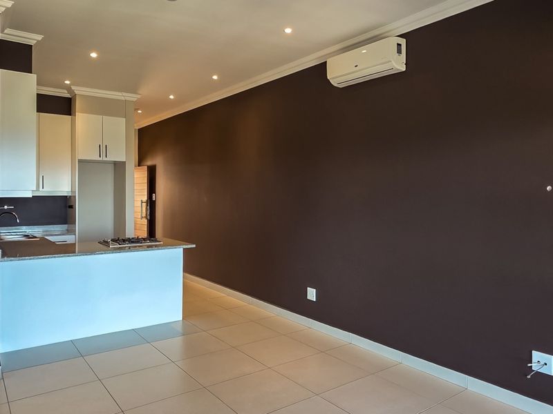 Open-plan living area featuring a modern kitchen with granite countertops, gas hob, tiled flooring, and a wall-mounted air conditioning unit.