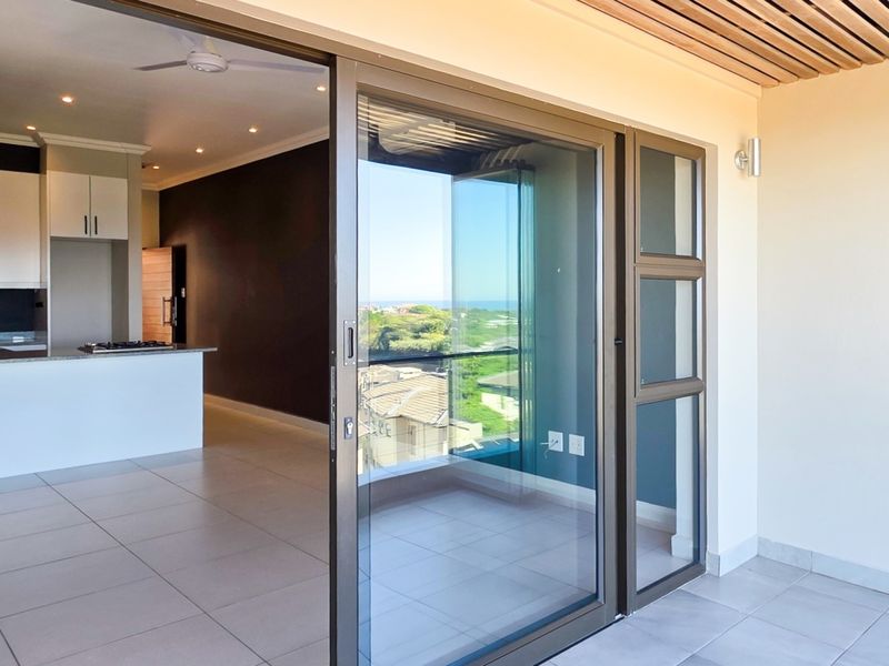 Modern open-plan apartment interior featuring tiled floors, a sleek kitchen with stone countertops, and large sliding doors opening onto a covered balcony.