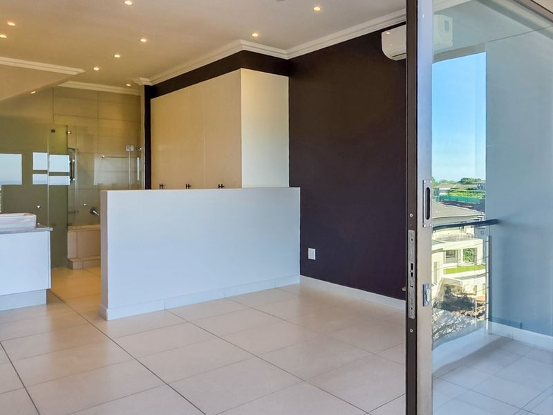 Spacious bedroom featuring an open-plan en-suite bathroom, built-in cupboards, tiled flooring, and direct access to a private balcony via sliding doors.