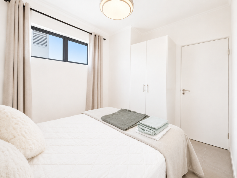A bright and clean bedroom featuring neutral tiled flooring, a built-in wardrobe, and a modern flush mount ceiling light.