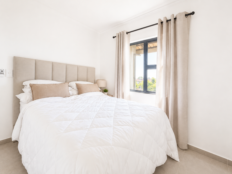A bright and well-maintained bedroom featuring neutral tiled flooring, a modern aluminium window frame, and clean white walls.