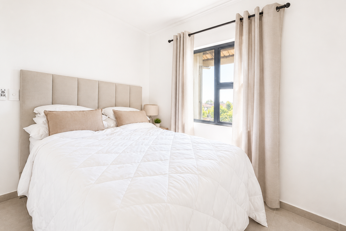 A bright and well-maintained bedroom featuring neutral tiled flooring, a modern aluminium window frame, and clean white walls.