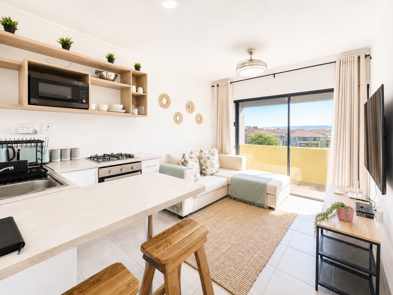 Modern open-plan apartment living area featuring a compact kitchen with built-in appliances, tiled floors, and direct access to a private balcony with scenic views.