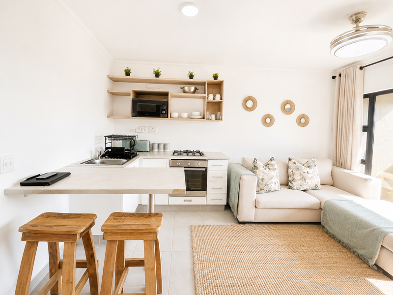 Modern open-plan living area featuring a compact kitchen with gas hob, built-in oven, stainless steel sink, and functional open shelving.