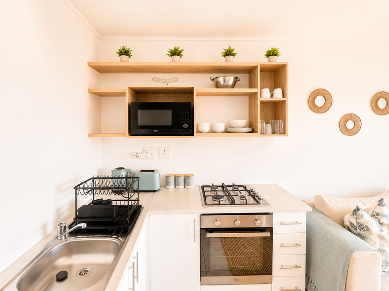 Compact open-plan kitchen area featuring built-in oven, gas hob, microwave, and open shelving, seamlessly integrated into the living space.
