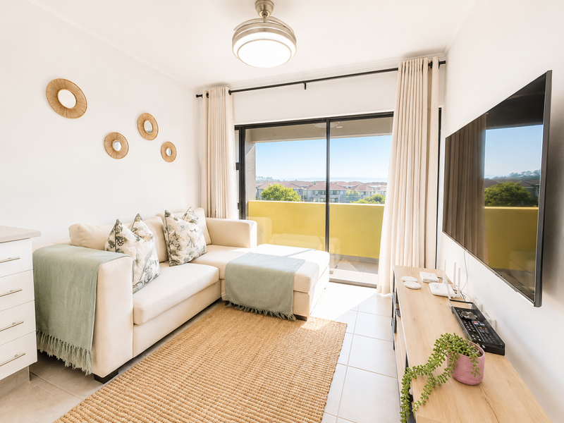 A bright and well-maintained living room featuring tiled flooring, a ceiling fan, and large sliding glass doors that open onto a balcony with scenic views.