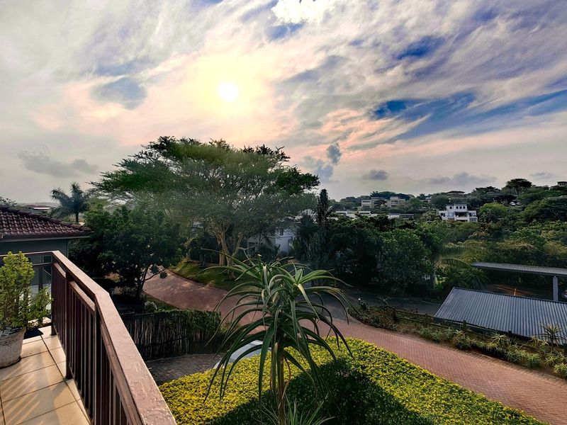A balcony with tiled flooring and a wooden balustrade, offering an elevated view of the surrounding neighbourhood and landscaped gardens.
