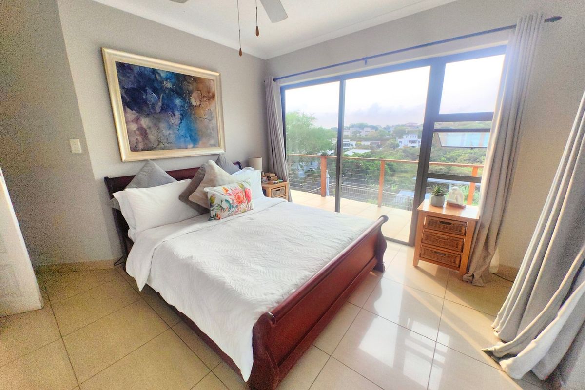 A bright bedroom featuring tiled flooring, a ceiling fan, and large sliding glass doors providing direct access to an outdoor balcony with scenic views.