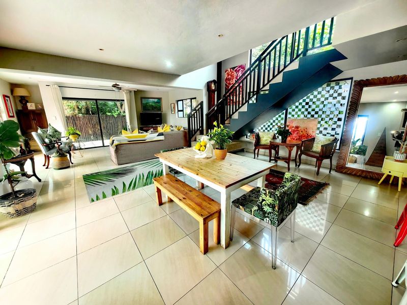 Spacious open-plan living and dining area featuring large format floor tiles, a modern staircase with metal balustrade, and sliding doors leading to the outdoors.
