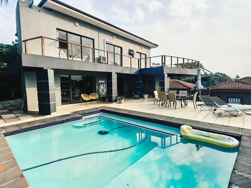 A spacious rear exterior featuring a swimming pool, expansive tiled patio area, and an upper-level balcony with modern architectural finishes.