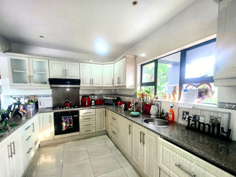 A functional kitchen featuring light-toned cabinetry, granite countertops, a gas hob with extractor, and tiled flooring with ample natural light.