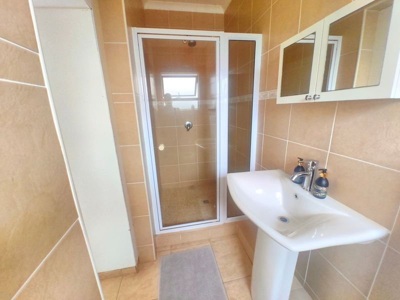 A functional bathroom featuring a pedestal sink, a glass-enclosed shower, and neutral-toned wall and floor tiling.