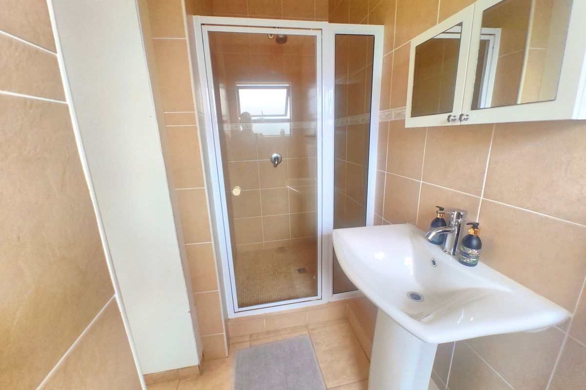 A functional bathroom featuring a pedestal sink, a glass-enclosed shower, and neutral-toned wall and floor tiling.