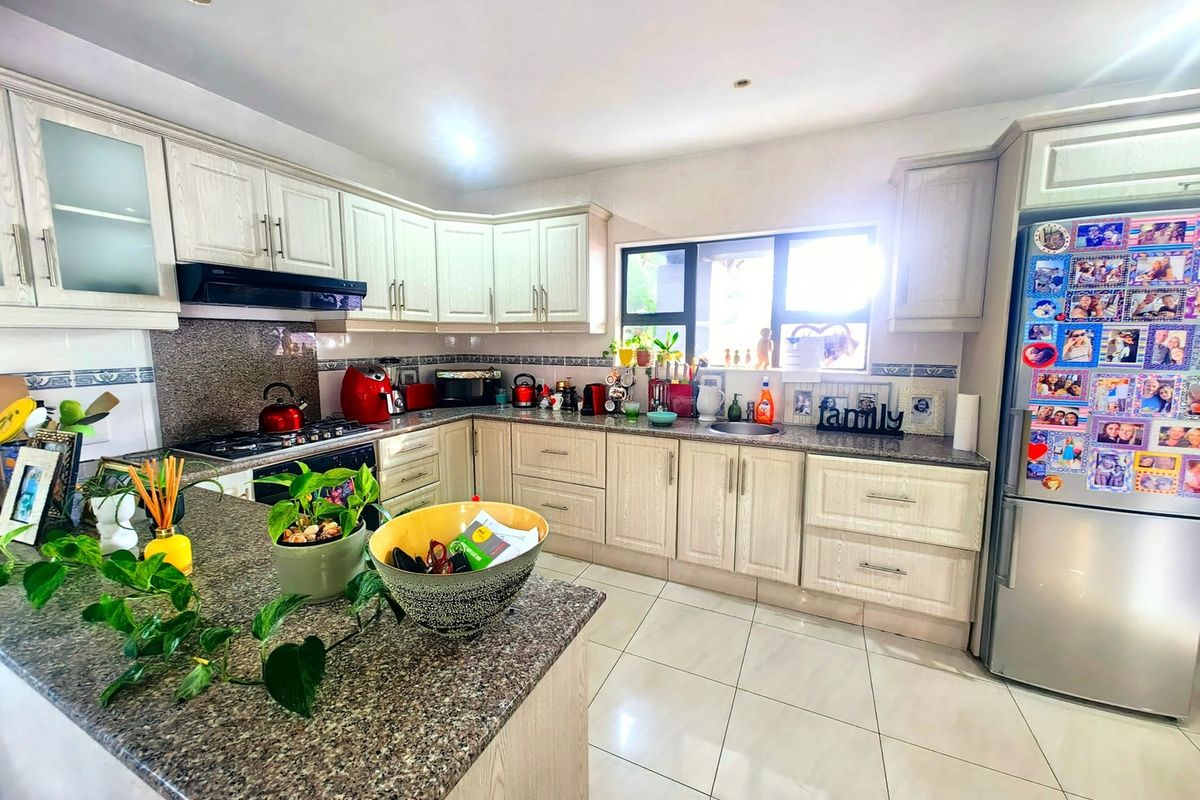 A functional kitchen featuring light-toned cabinetry, granite countertops, a gas hob with extractor fan, and tiled flooring, offering ample workspace and storage.