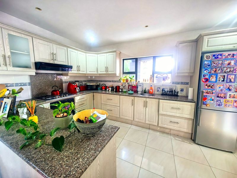 A functional kitchen featuring light-toned cabinetry, granite countertops, a gas hob with extractor fan, and tiled flooring, offering ample workspace and storage.