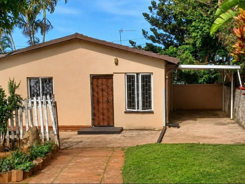 Front elevation of a cottage featuring a paved driveway, attached carport, security gate, and a small front garden with a picket fence.