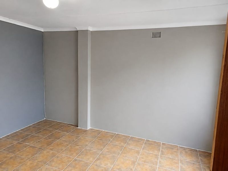 An empty bedroom featuring neutral grey painted walls, tiled flooring, and a ceiling cornice.