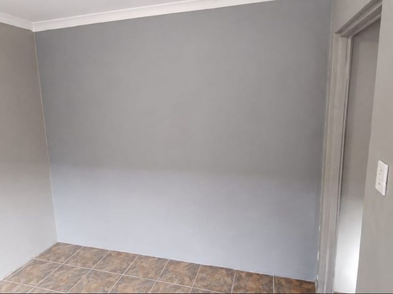 A clean, empty bedroom featuring neutral grey walls, tiled flooring, and coving detail, providing a blank canvas for interior design.