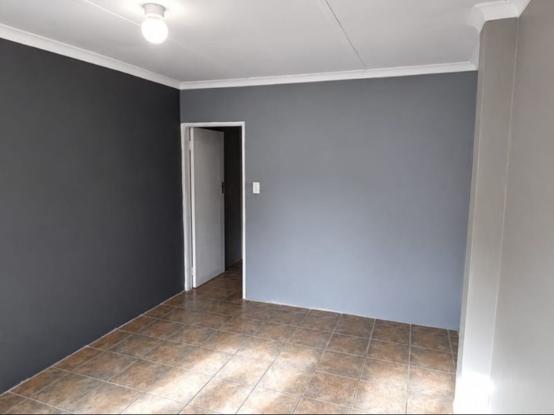 An empty bedroom featuring tiled flooring, neutral grey painted walls, and a coved ceiling, providing a clean and versatile space.