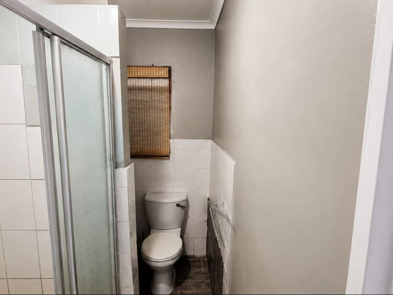 A functional bathroom featuring a shower enclosure and toilet with tiled finishes, offering a clean but dated aesthetic ready for modernization.