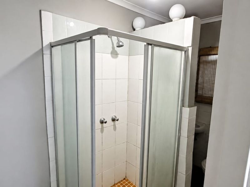 A functional bathroom featuring a corner shower enclosure with tiled walls and floor, complemented by wall-mounted lighting.