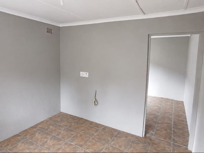 An empty living area featuring neutral grey walls, tiled flooring, and an exposed electrical point, offering a blank canvas for interior design.