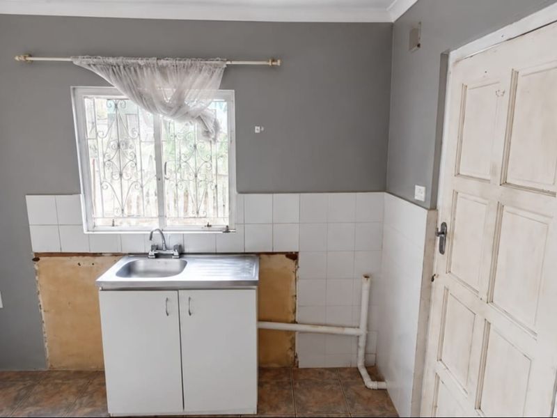 A compact kitchen area featuring a single sink unit, tiled splashback, and tiled flooring, currently requiring cabinetry completion and cosmetic updates.