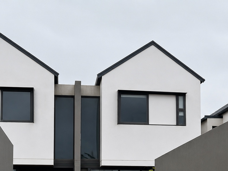 A modern townhouse exterior featuring clean lines, gabled roof profiles, and contemporary dark-framed windows against a crisp white facade.