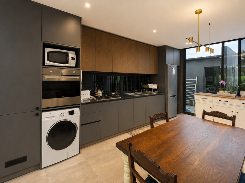 Modern open-plan kitchen featuring dark grey cabinetry, wood-grain upper cupboards, integrated appliances, and large windows providing natural light and garden access.