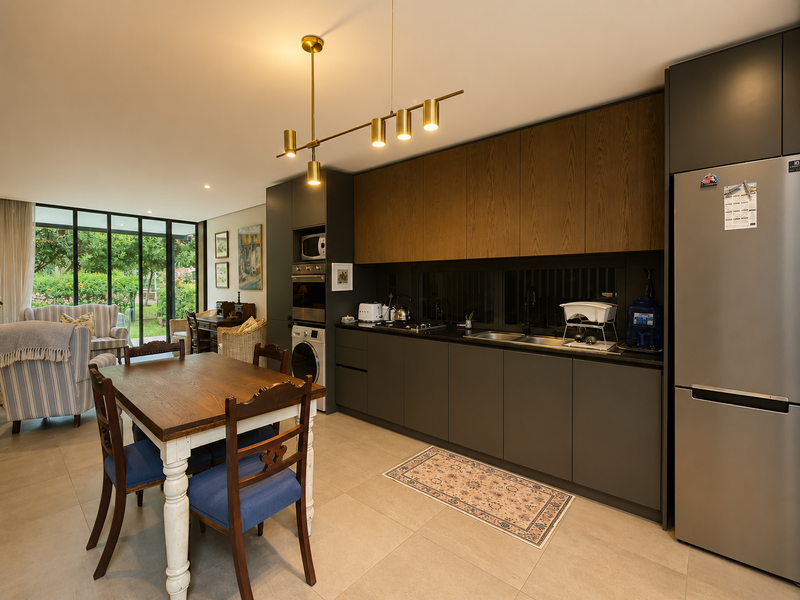 Modern open-plan kitchen and dining area featuring sleek dark cabinetry, integrated appliances, tiled floors, and large glass doors opening to the garden.