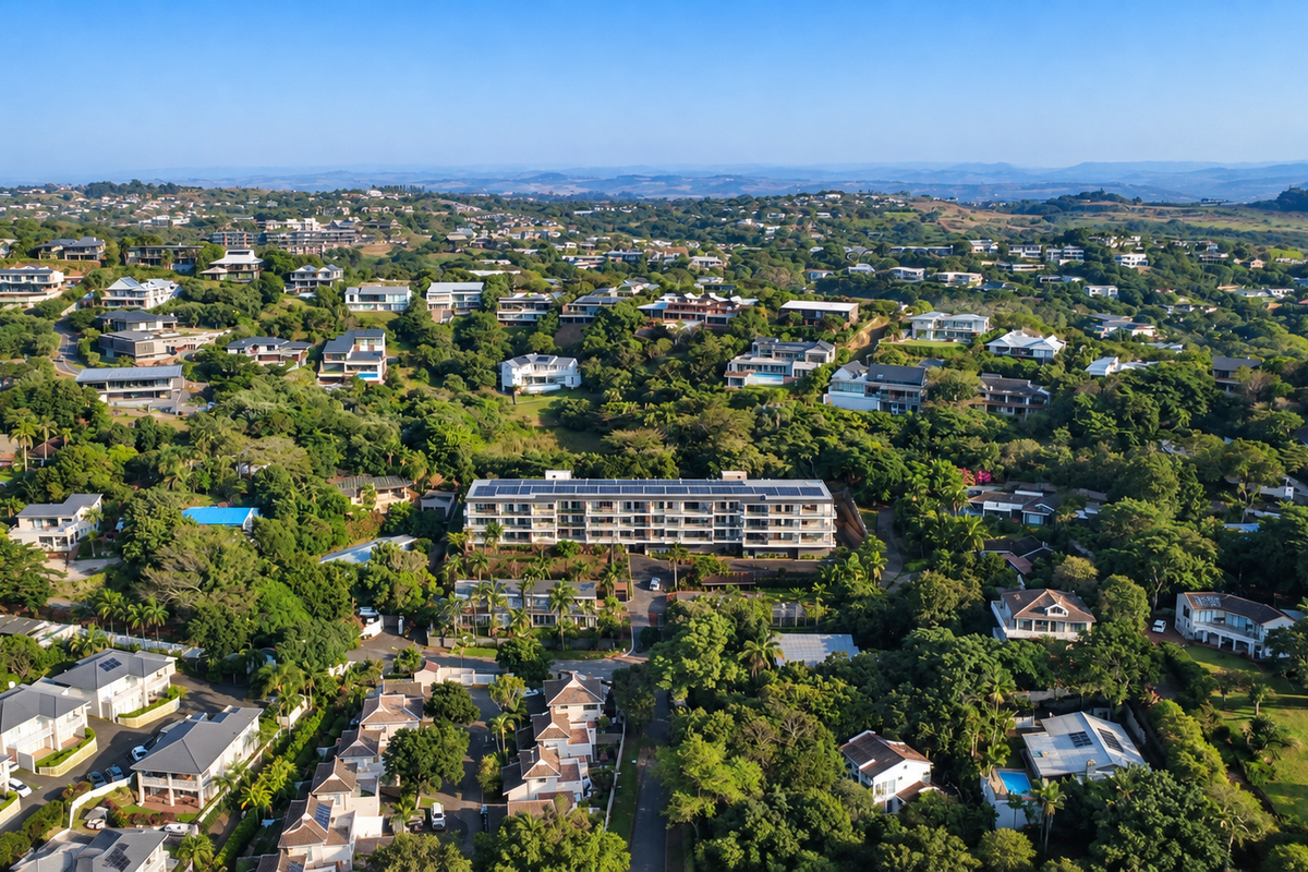 An aerial view of the apartment complex surrounded by lush greenery and residential neighborhood, featuring solar panels installed on the roof.