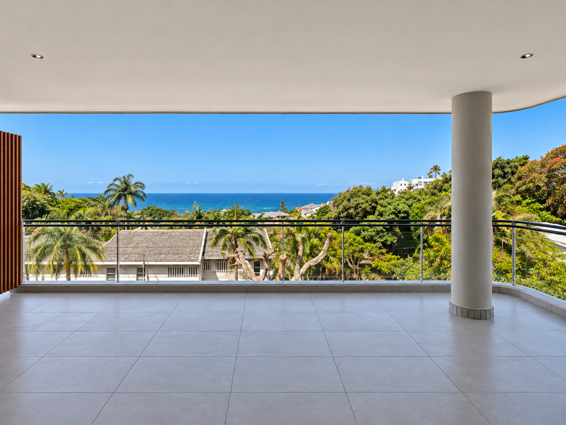 Spacious covered balcony featuring modern tiled flooring, a sleek glass balustrade, and expansive ocean views.