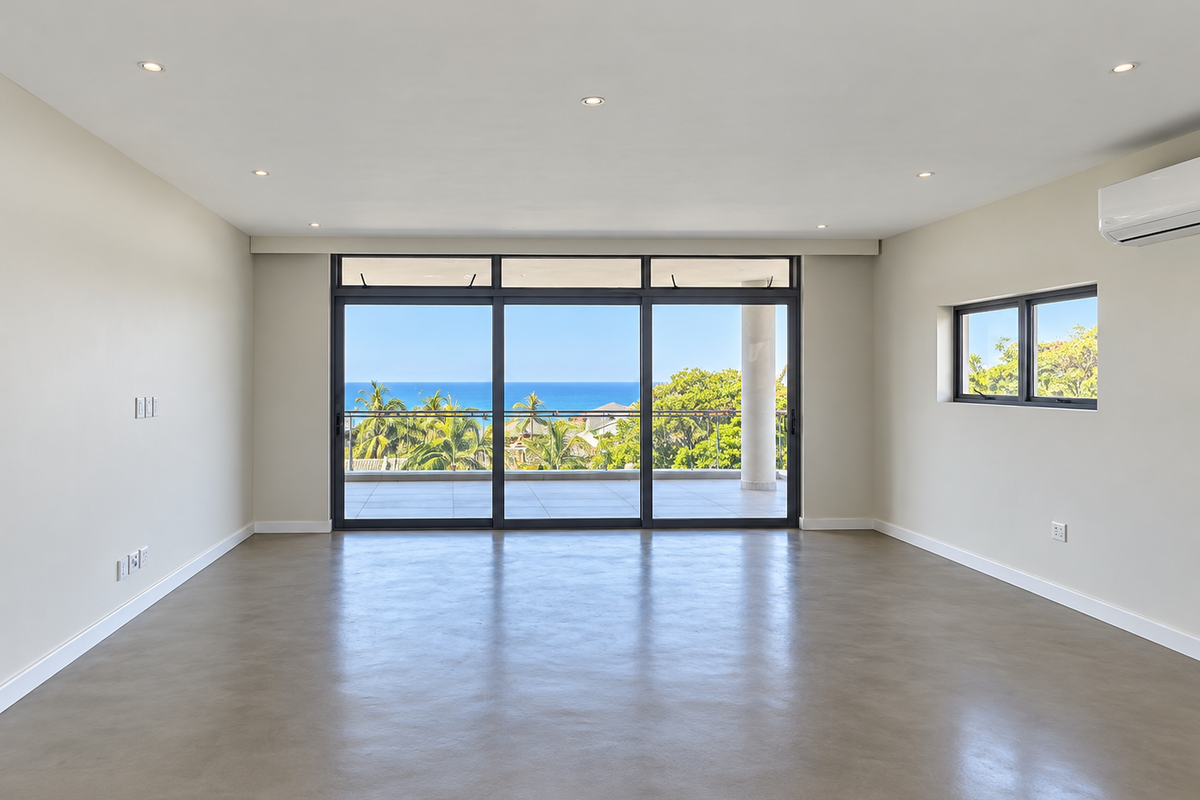 Spacious, light-filled living area featuring polished concrete floors, recessed lighting, and large sliding glass doors opening to a balcony with ocean views.