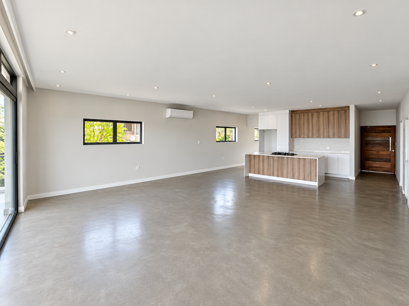 Spacious open-plan living area featuring polished concrete floors, recessed lighting, and a modern kitchen with a central island and built-in cabinetry.