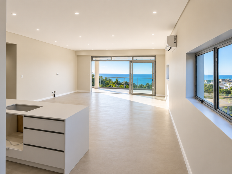 Spacious open-plan living area featuring a modern kitchen island, neutral tiled flooring, and large sliding doors opening to a balcony with ocean views.