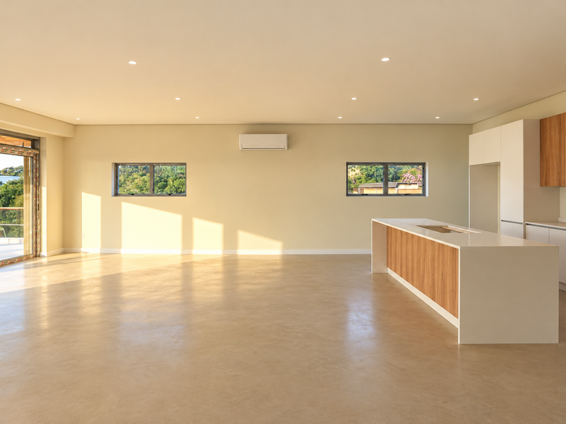 Spacious open-plan living and kitchen area featuring modern cabinetry, a central island, polished concrete floors, and large sliding doors leading to an outdoor space.