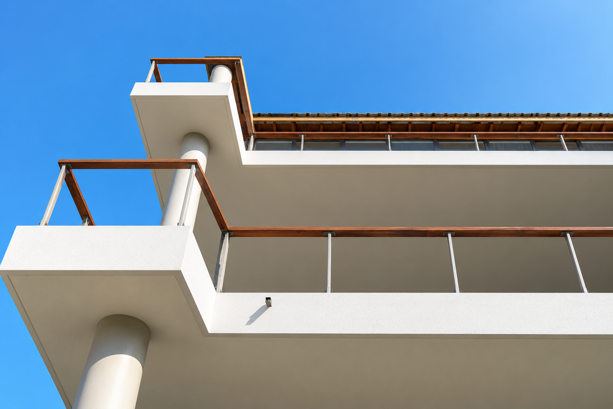 Low angle view of modern apartment building balconies featuring clean white concrete finishes, wooden handrails, and structural support columns against a clear blue sky.